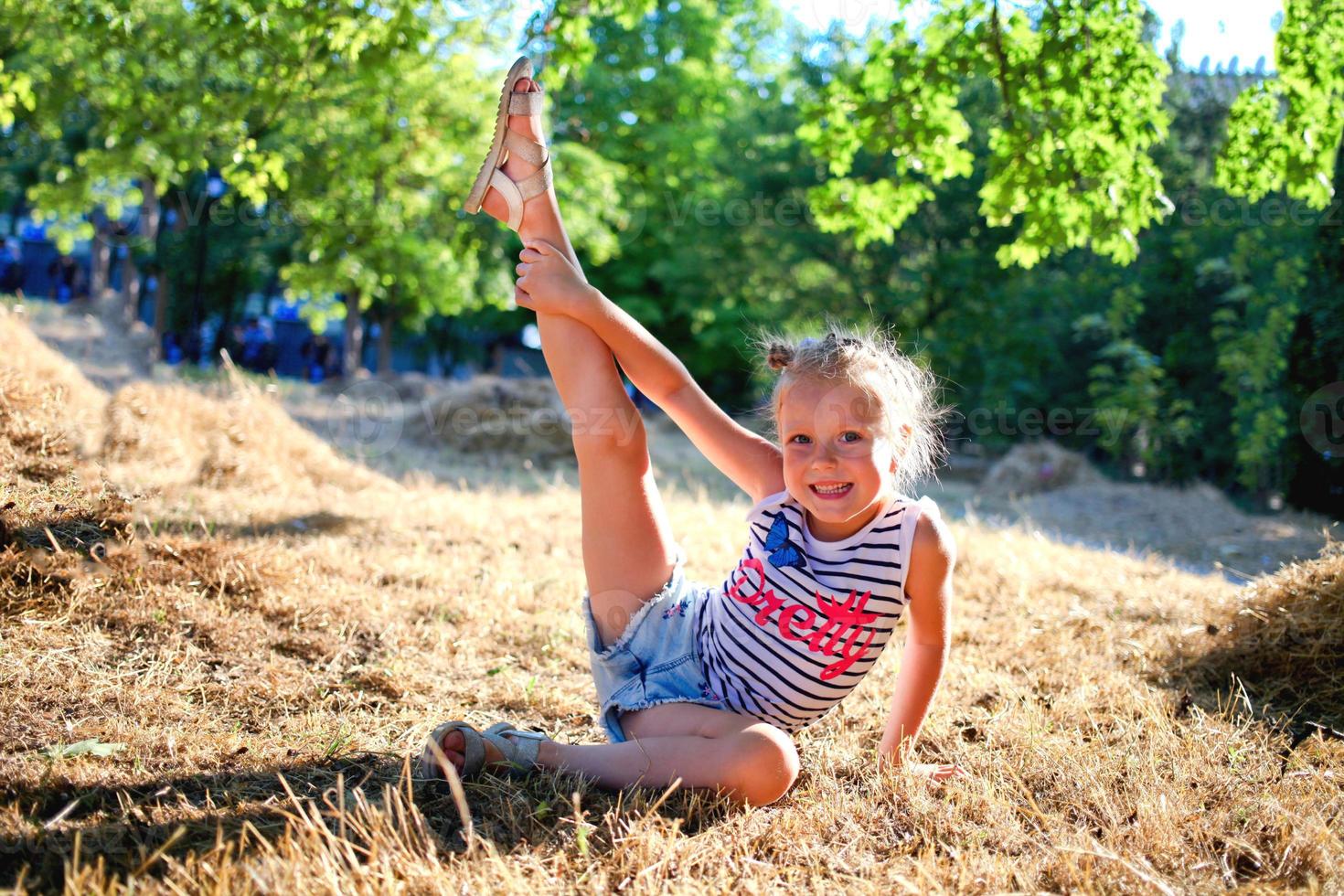 el pequeño niña levanta su pierna arriba, gimnasia ejercicios en naturaleza. flexible niño, aptitud física, extensión, yoga, Deportes, aprendiendo. foto