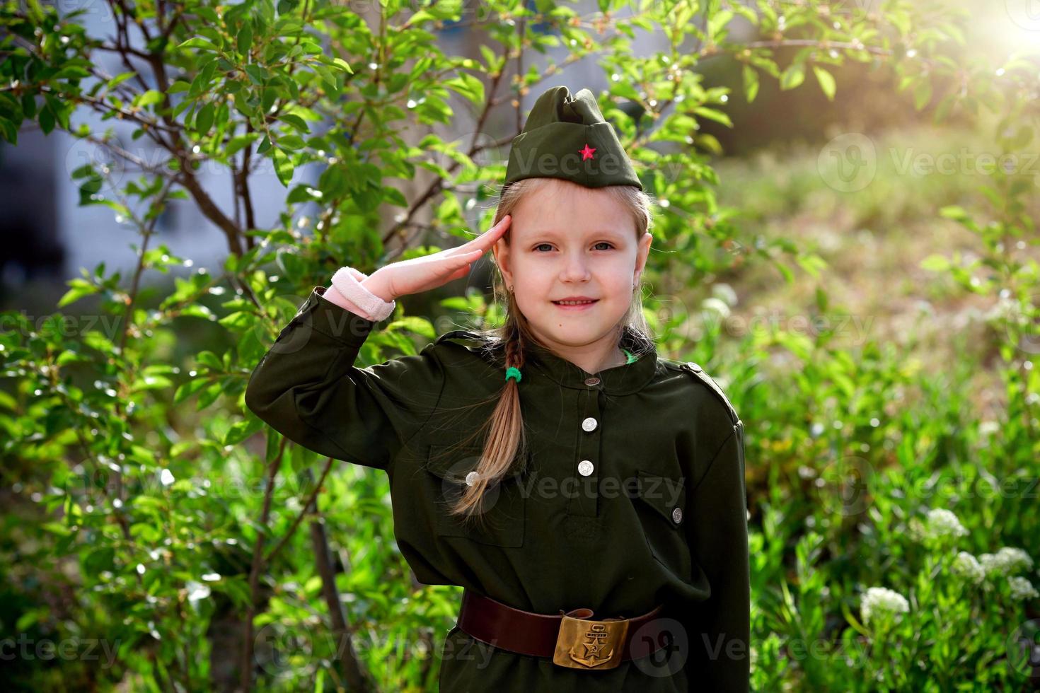 Portrait happy girl in uniform put a hand to her head on a green background. Victory Day. photo
