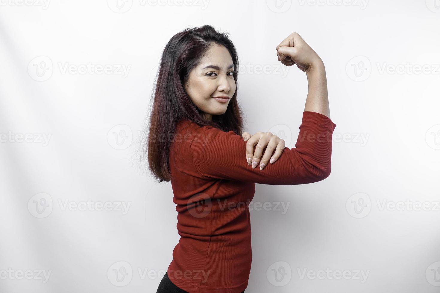 Excited Asian woman wearing a red top showing strong gesture by lifting her arms and muscles smiling proudly photo