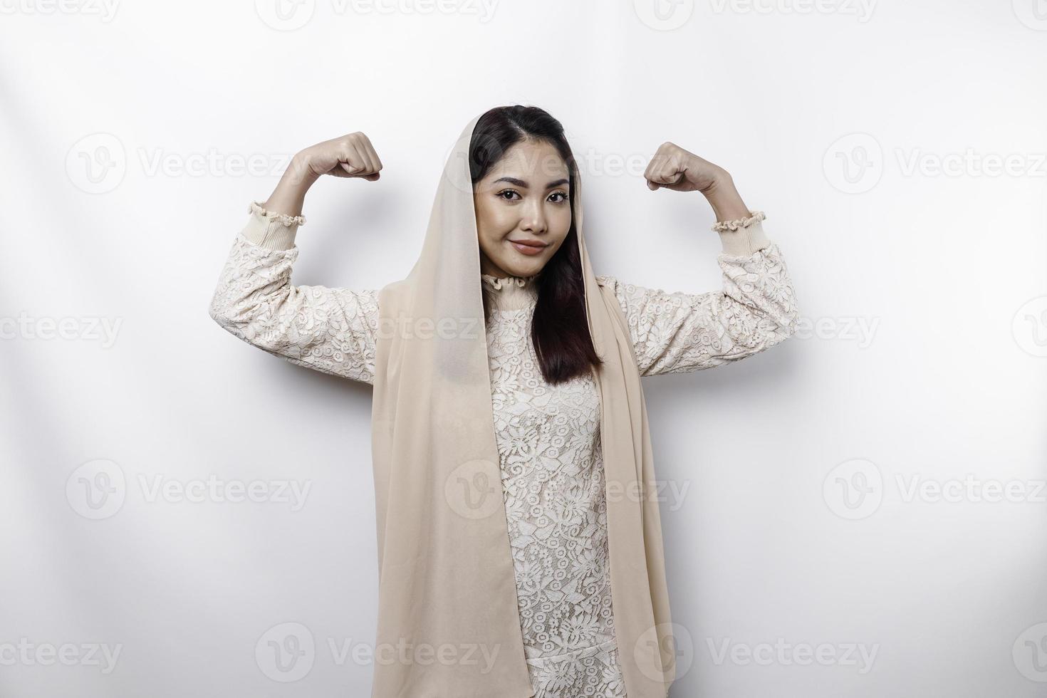 Excited Asian Muslim woman wearing a headscarf showing strong gesture by lifting her arms and muscles smiling proudly photo