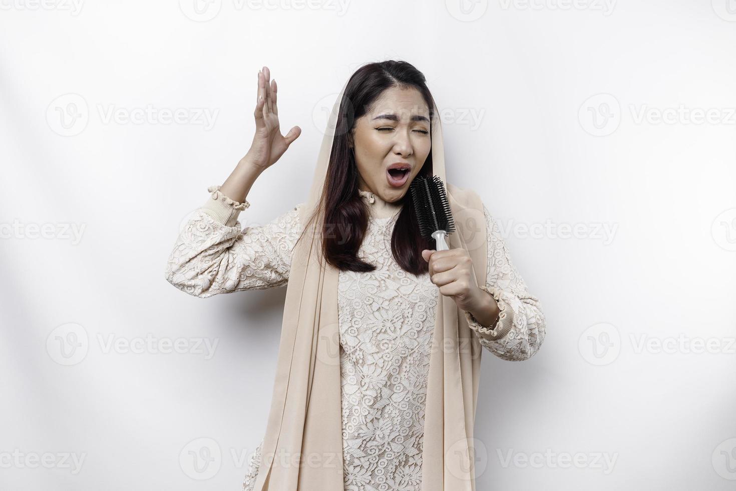 Portrait of carefree Asian Muslim woman, having fun karaoke, singing in microphone while standing over white background photo