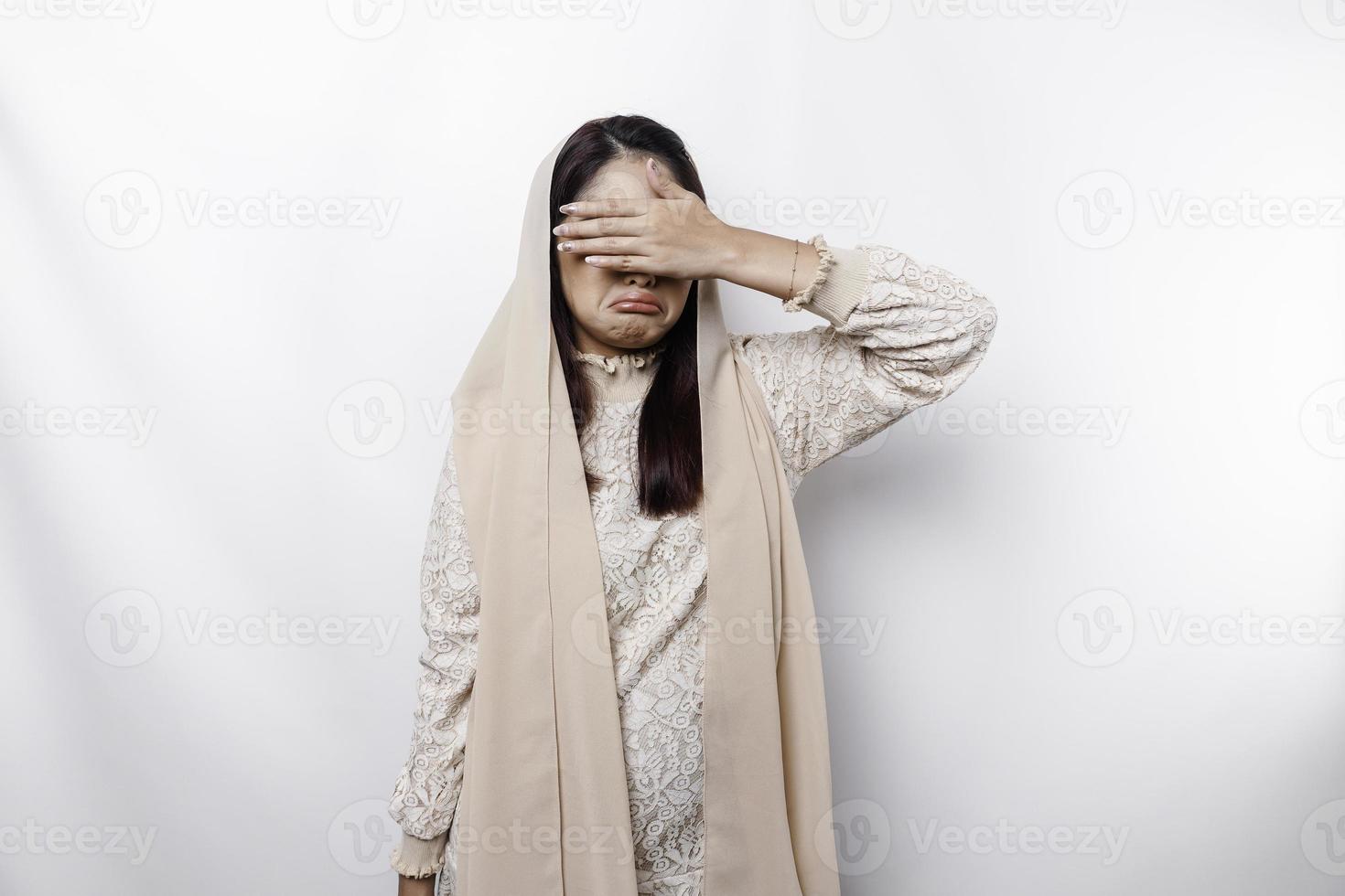 Young Asian Muslim woman isolated on white background, looks depressed, face covered by arms frightened and nervous. photo