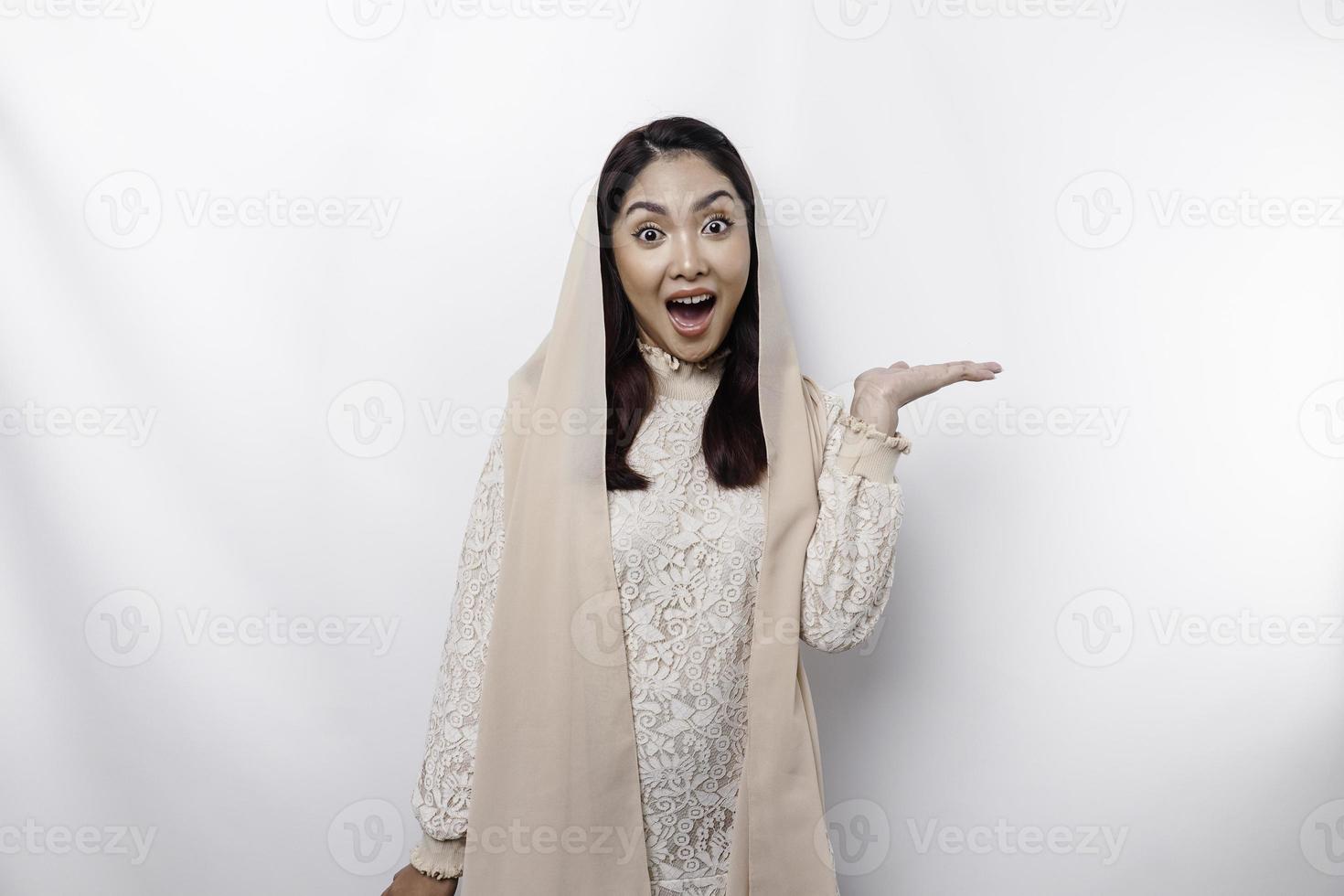 Shocked Asian Muslim woman pointing at the copy space on beside her, isolated by white background photo