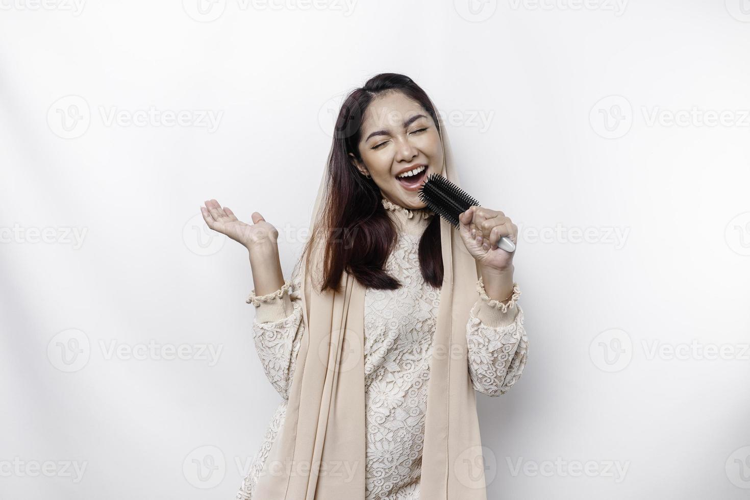 Portrait of carefree Asian Muslim woman, having fun karaoke, singing in microphone while standing over white background photo