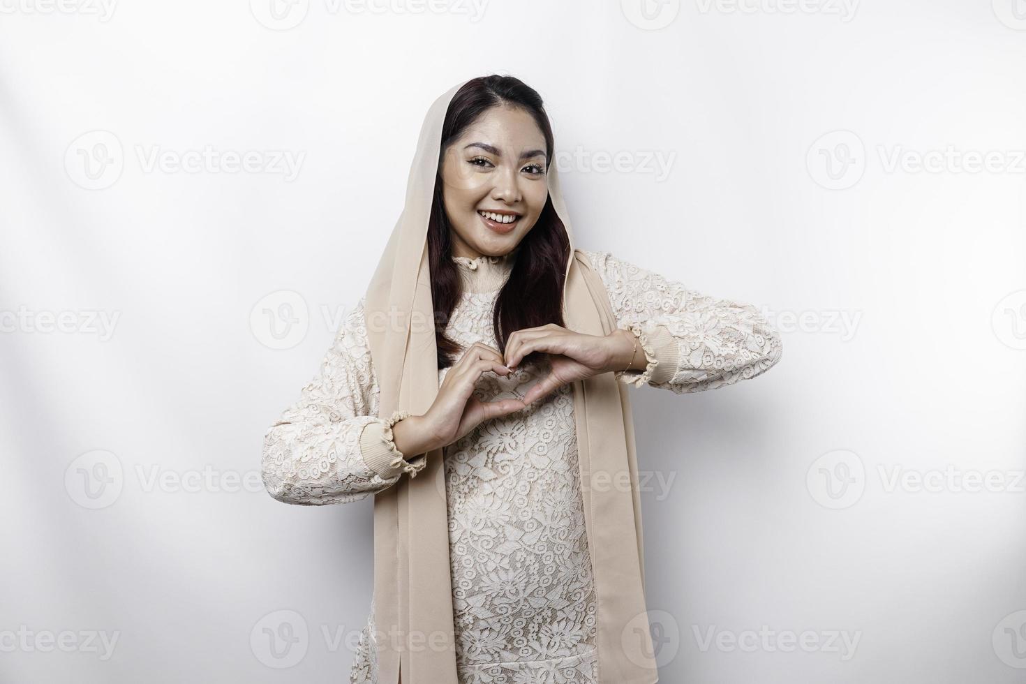 A happy young Asian woman wearing headscarf feels romantic shapes heart gesture expresses tender feelings photo