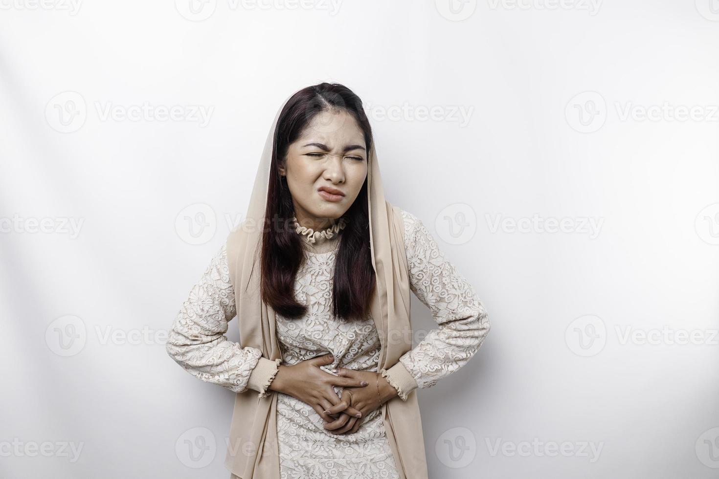 An Asian Muslim woman is fasting and hungry and touching her belly while looking aside thinking about what to eat photo