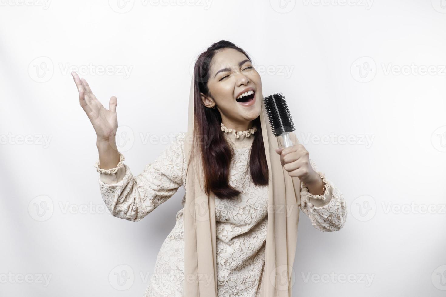 Portrait of carefree Asian Muslim woman, having fun karaoke, singing in microphone while standing over white background photo