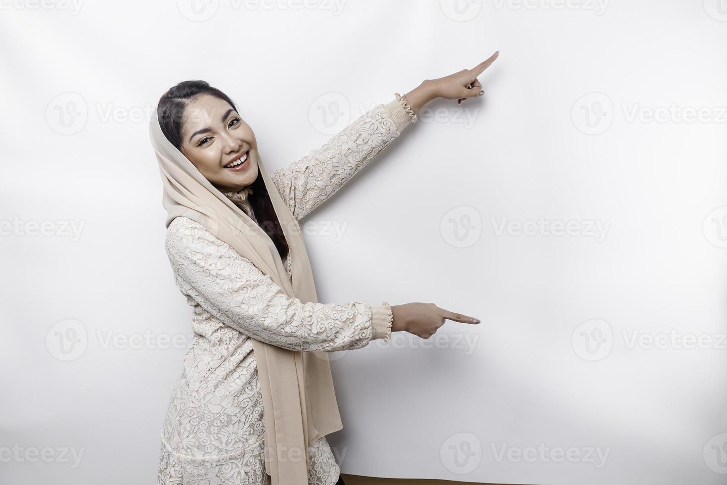 Young Asian Muslim woman smiling while pointing to copy space beside her photo