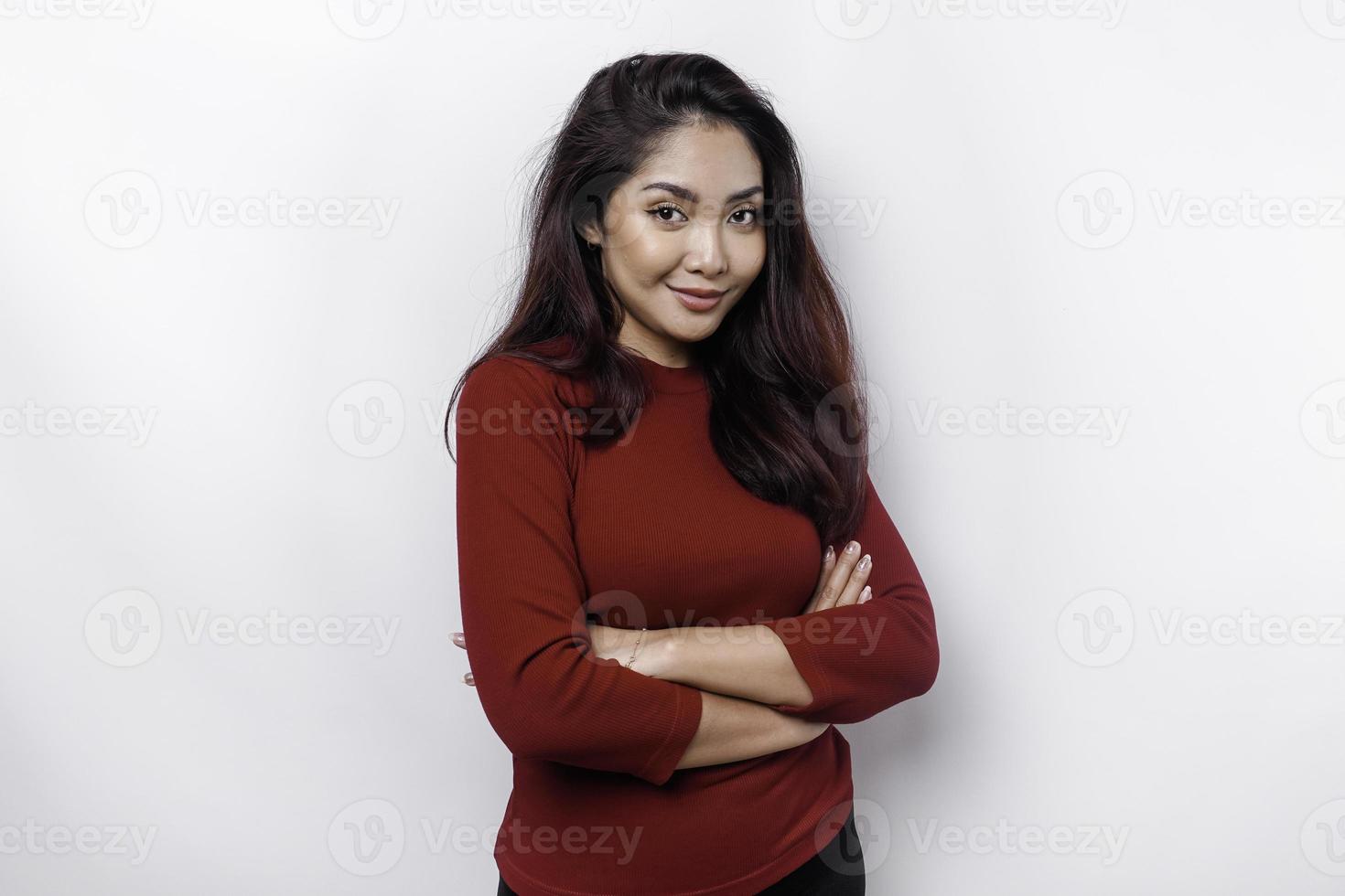 retrato de un confidente sonriente asiático mujer vestido en rojo, en pie con brazos doblada y mirando a el cámara aislado terminado blanco antecedentes foto