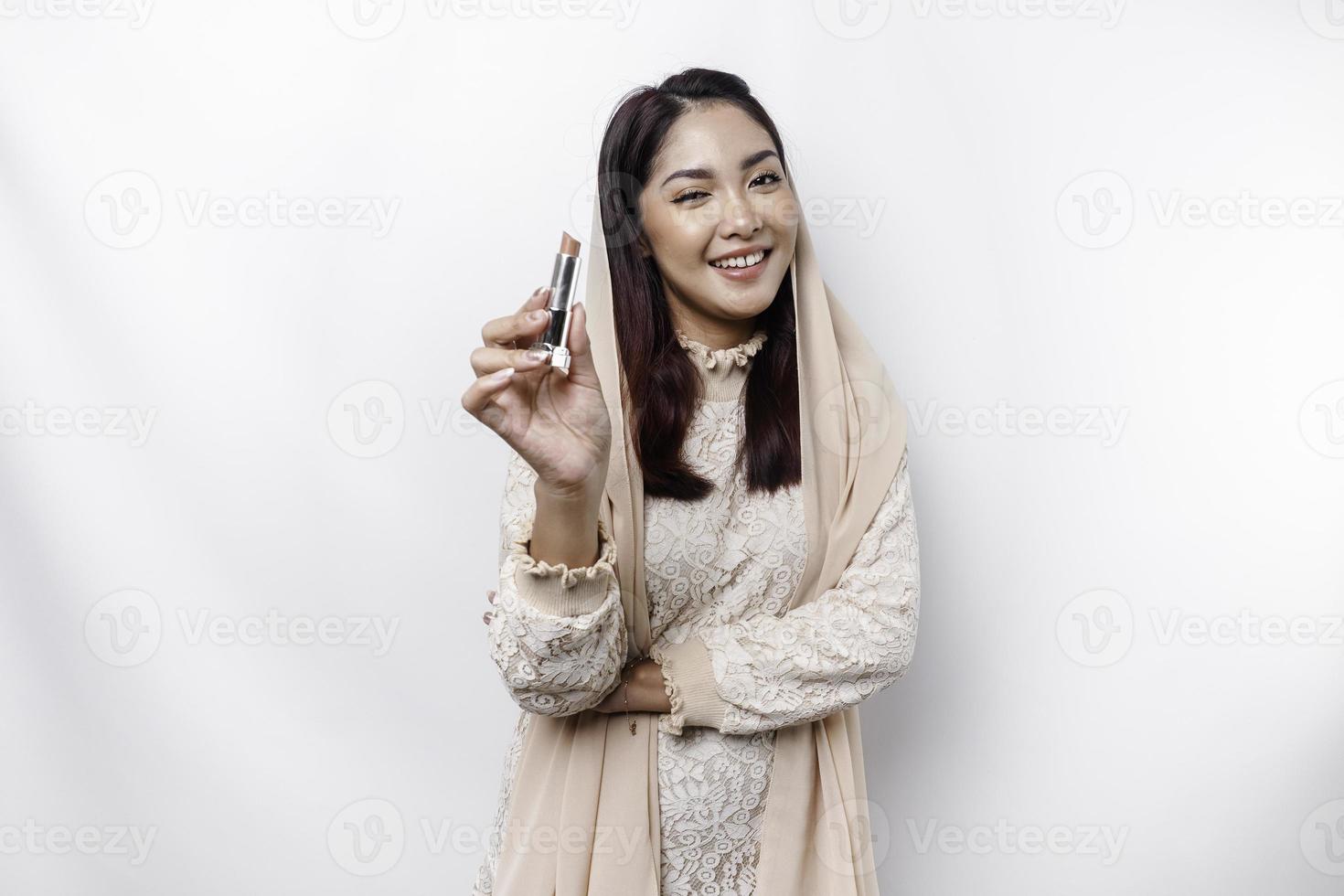 Portrait of a young beautiful Asian Muslim woman wearing a headscarf holding her lipstick photo