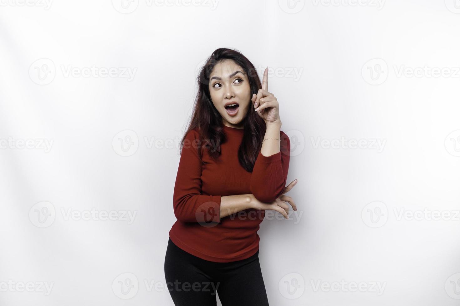 Shocked Asian woman dressed in red, pointing at the copy space above her, isolated by white background photo