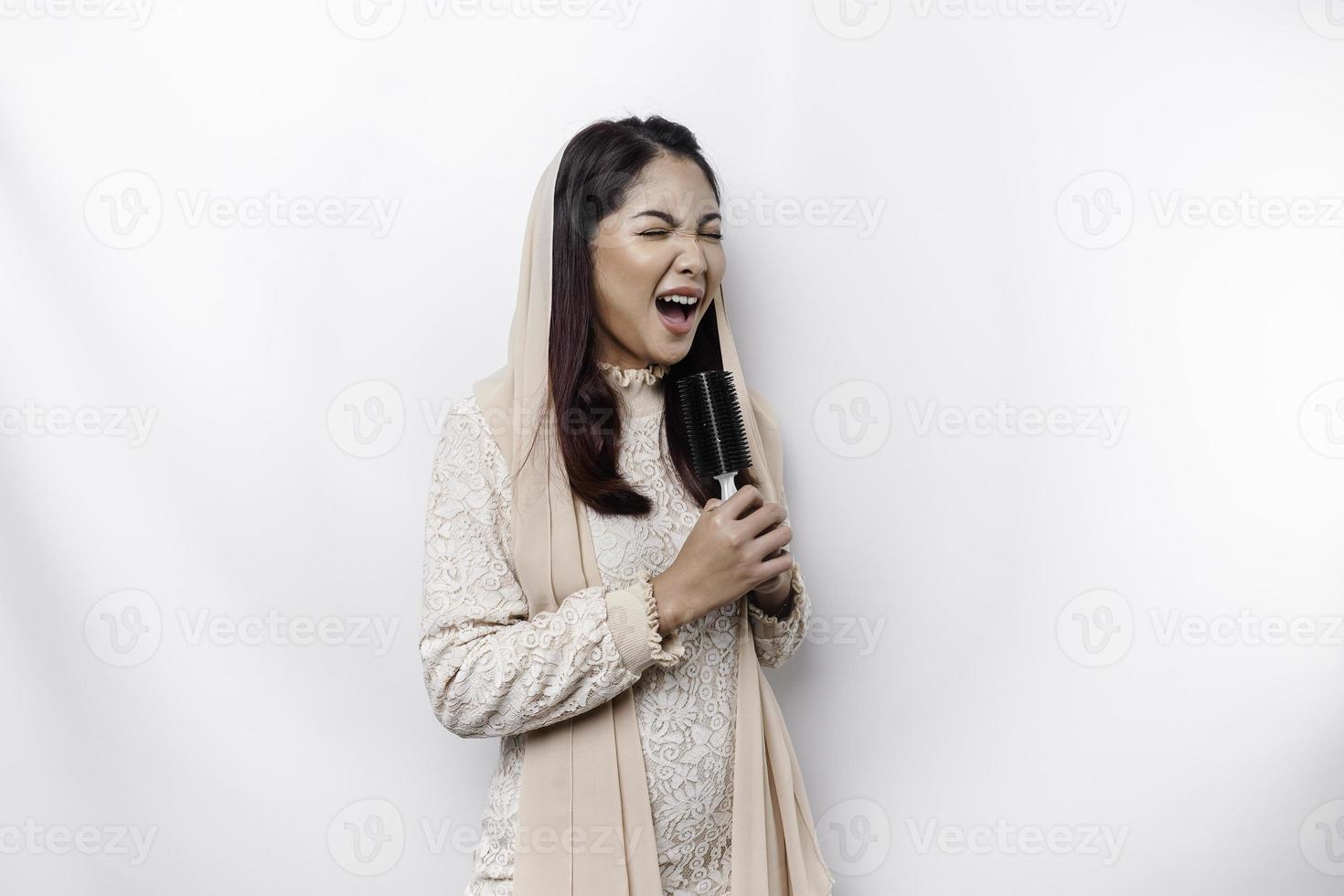 Portrait of carefree Asian Muslim woman, having fun karaoke, singing in microphone while standing over white background photo