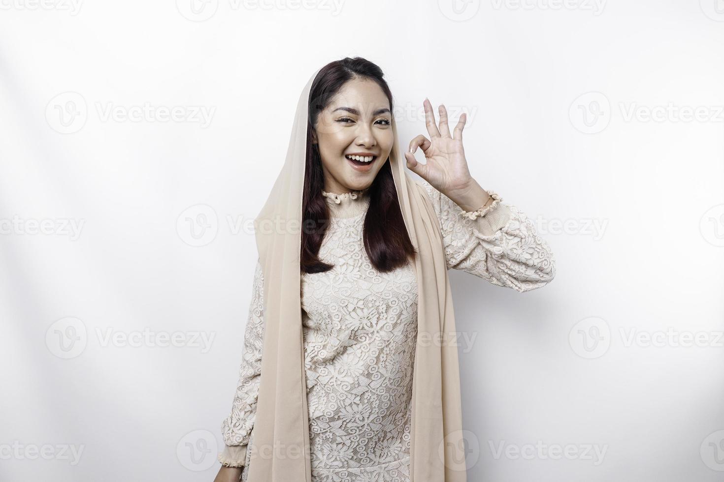 Portrait of a smiling Asian Muslim woman, giving an OK hand gesture isolated over white background photo