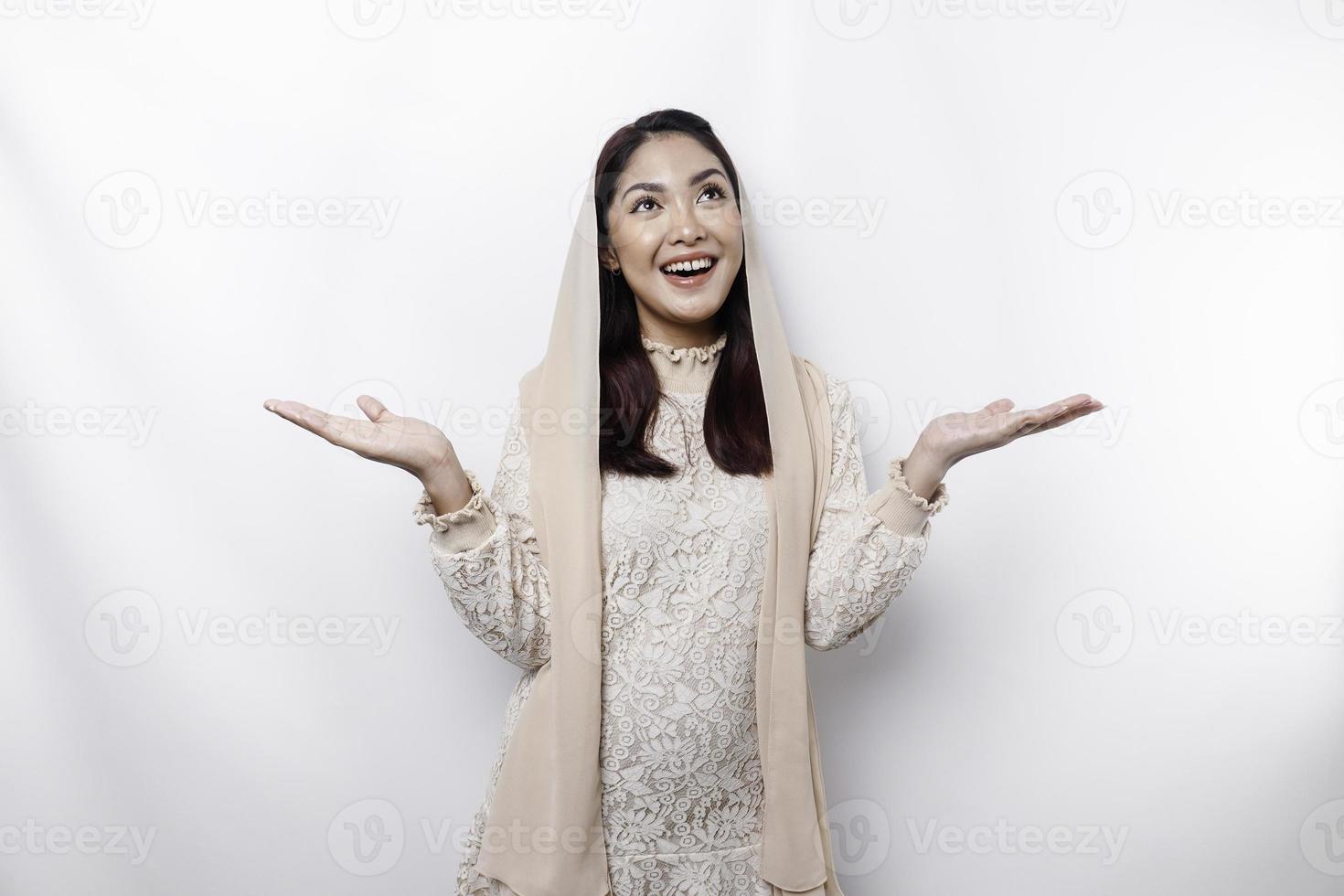 Young Asian Muslim woman smiling while pointing to copy space beside her photo