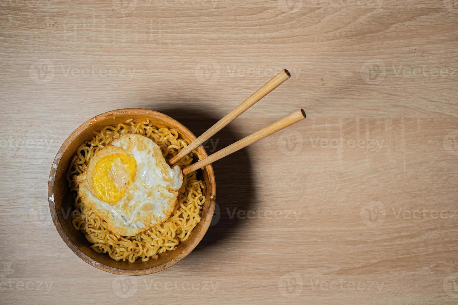 Fried Noodles and Sunny-Side Up Egg with Chopsticks on a Wooden Bowl and Wooden Table photo