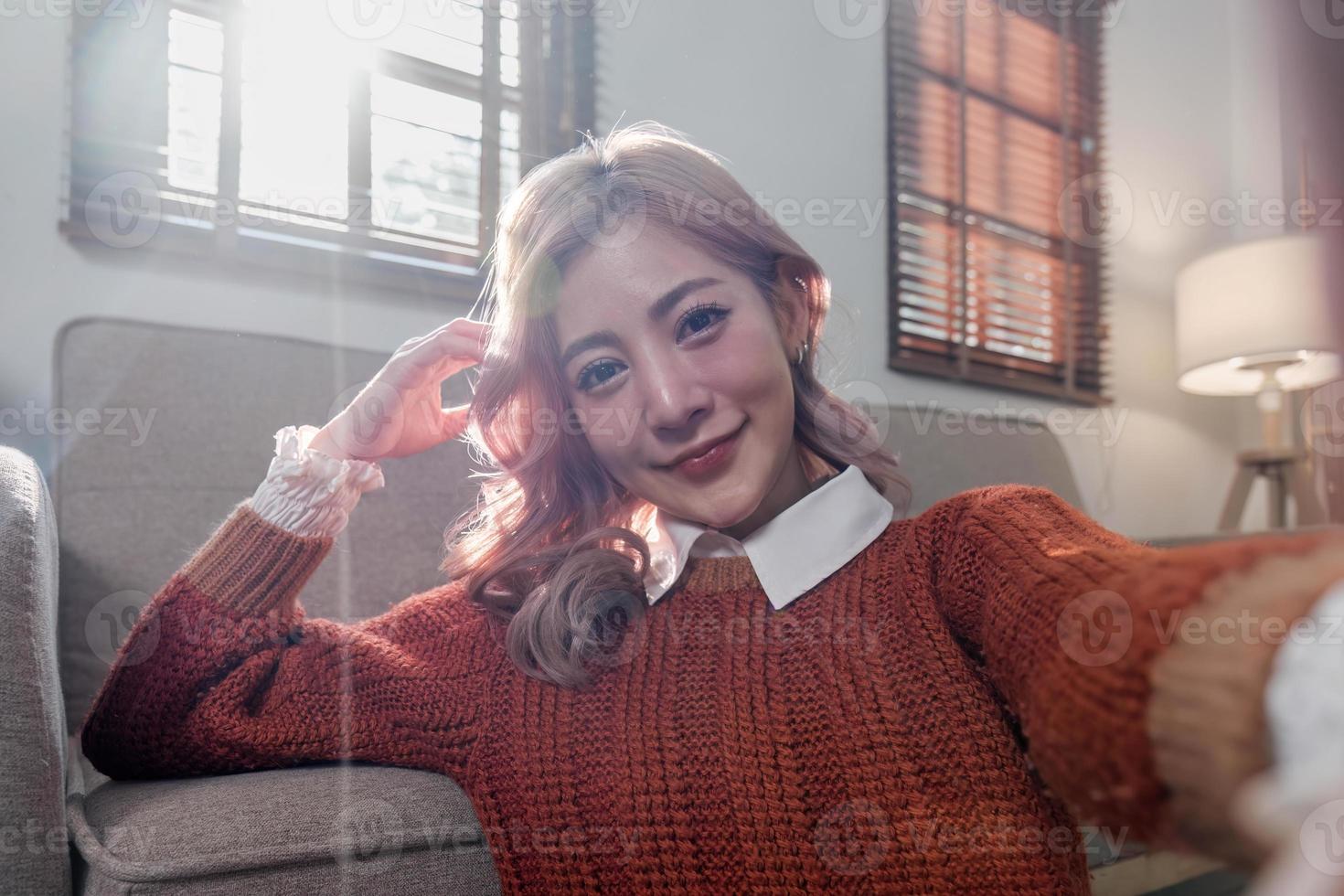 joven hermosa asiático mujer relajante en vivo habitación a hogar, leyendo libros, Bebiendo café y utilizando teléfono en el Mañana con contento sensación foto
