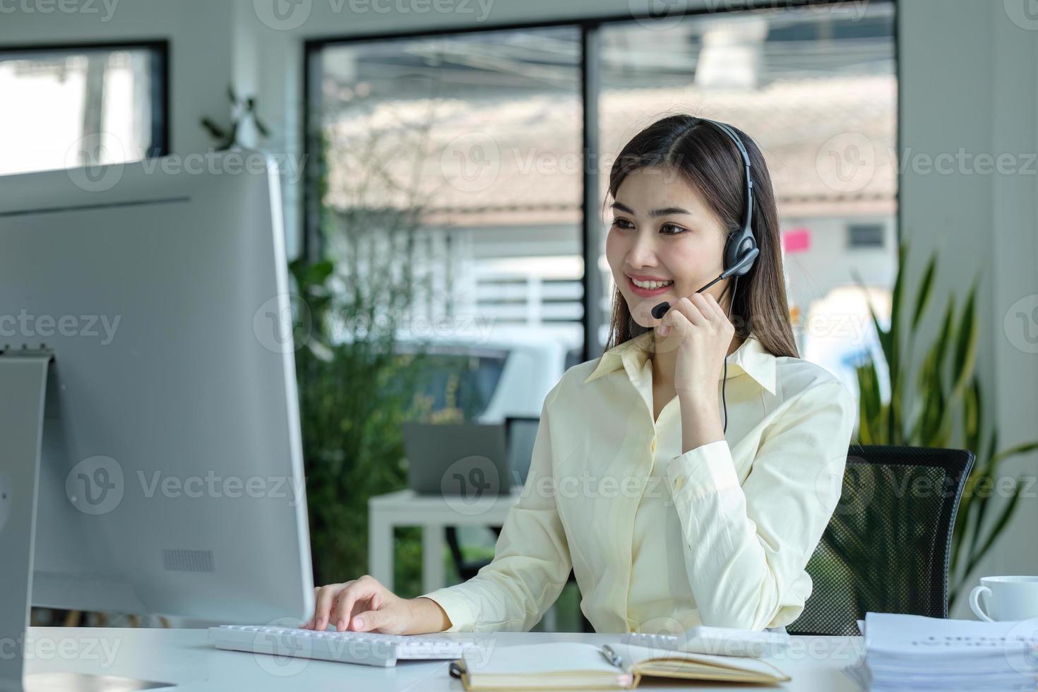 close up call center operator in wireless headset talking with customer, woman in headphones with microphone consulting client on phone in customer support service, looking at computer screen photo