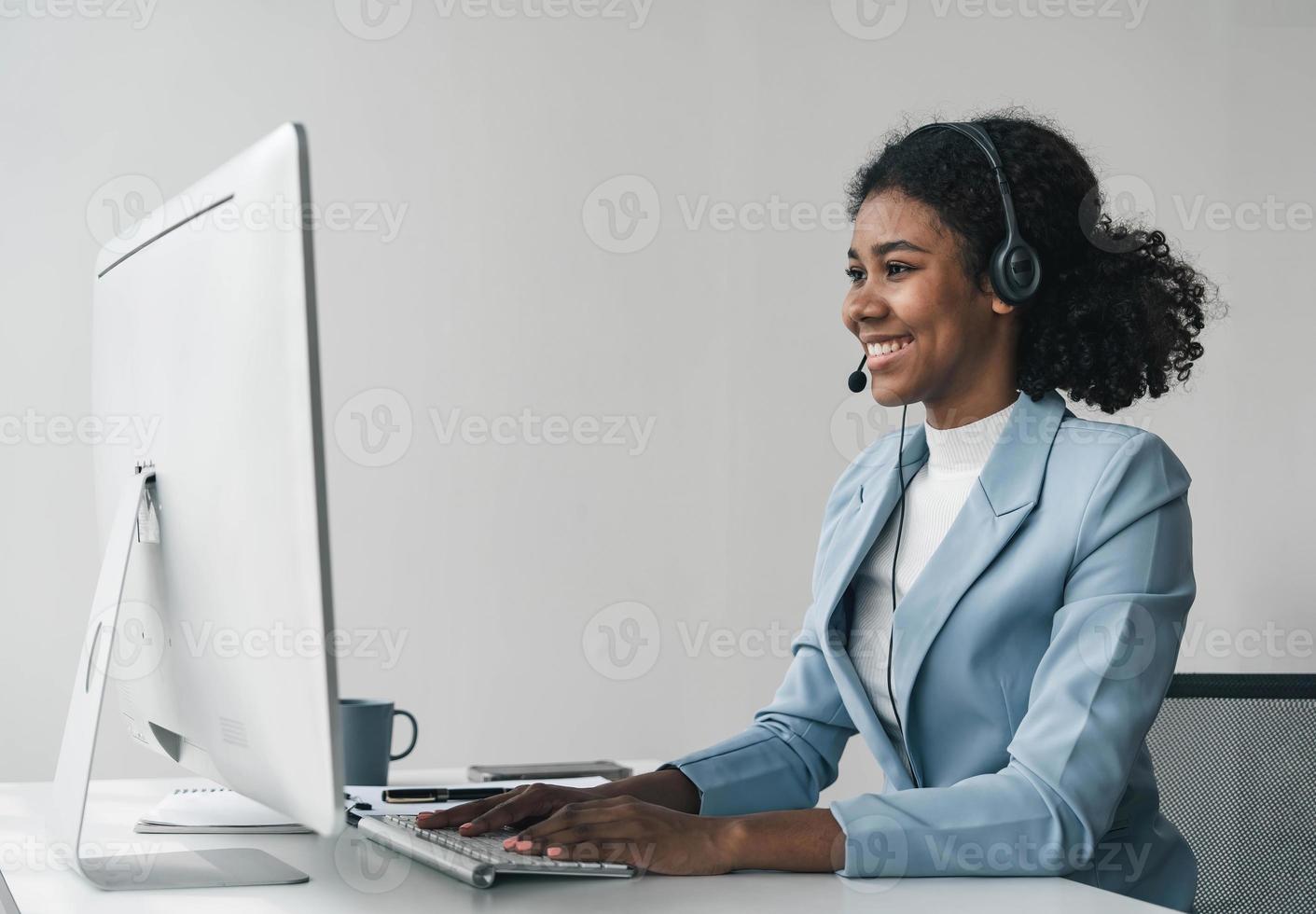 close up call center operator in wireless headset talking with customer, woman in headphones with microphone consulting client on phone in customer support service, looking at computer screen photo