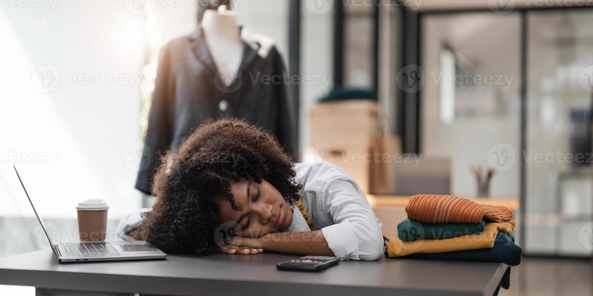 People tailor working in fashion design concept. Young adult asian designer woman tried and sleeping at workshop table. Background in business start up studio dressmaker. photo