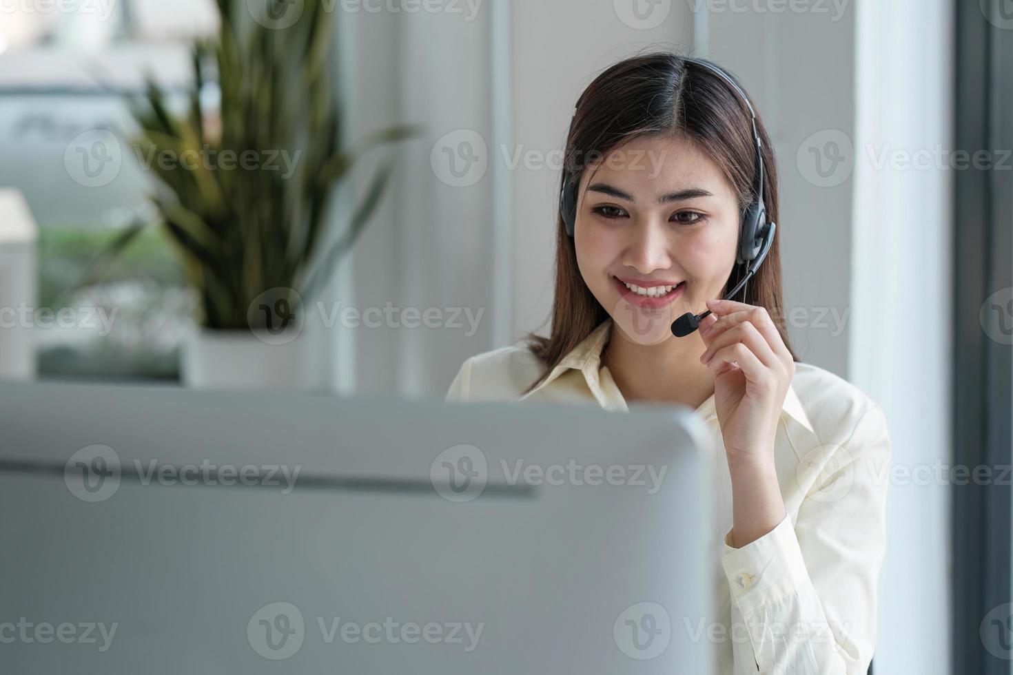 close up call center operator in wireless headset talking with customer, woman in headphones with microphone consulting client on phone in customer support service, looking at computer screen photo