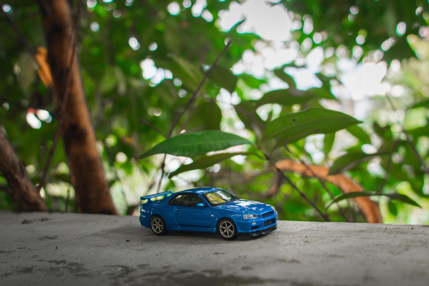 Concept for nature adventure. After some edits, a photo of blue toy car placed near a tree.