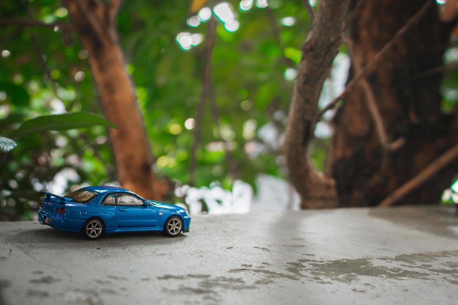 Concept for nature adventure. After some edits, a photo of blue toy car placed near a tree.