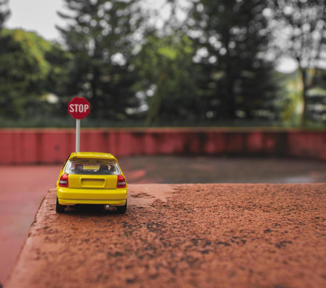 A yellow toy car meets a stop sign in the park. photo