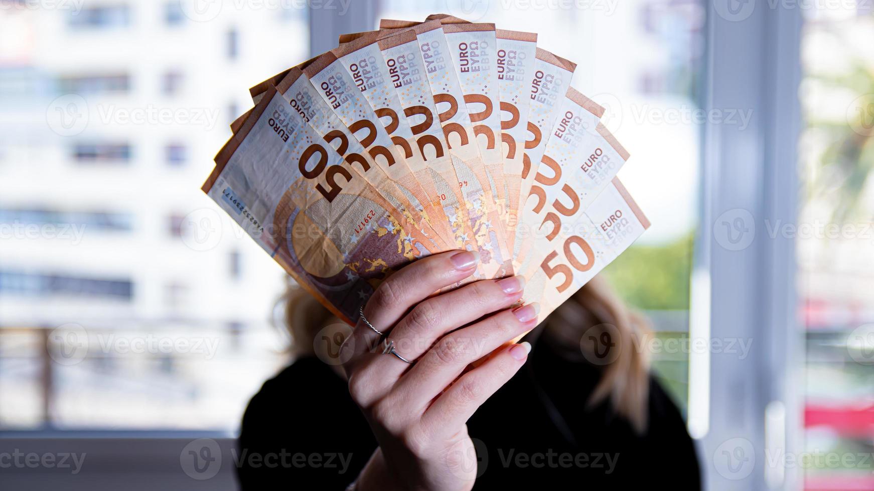 Woman's hand holding a fan of euro banknotes on a black background photo