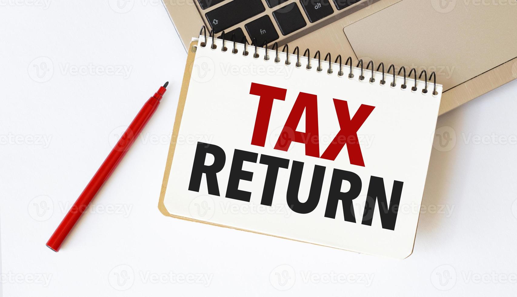 Laptop, red pen and notepad with text tax return in the white background photo