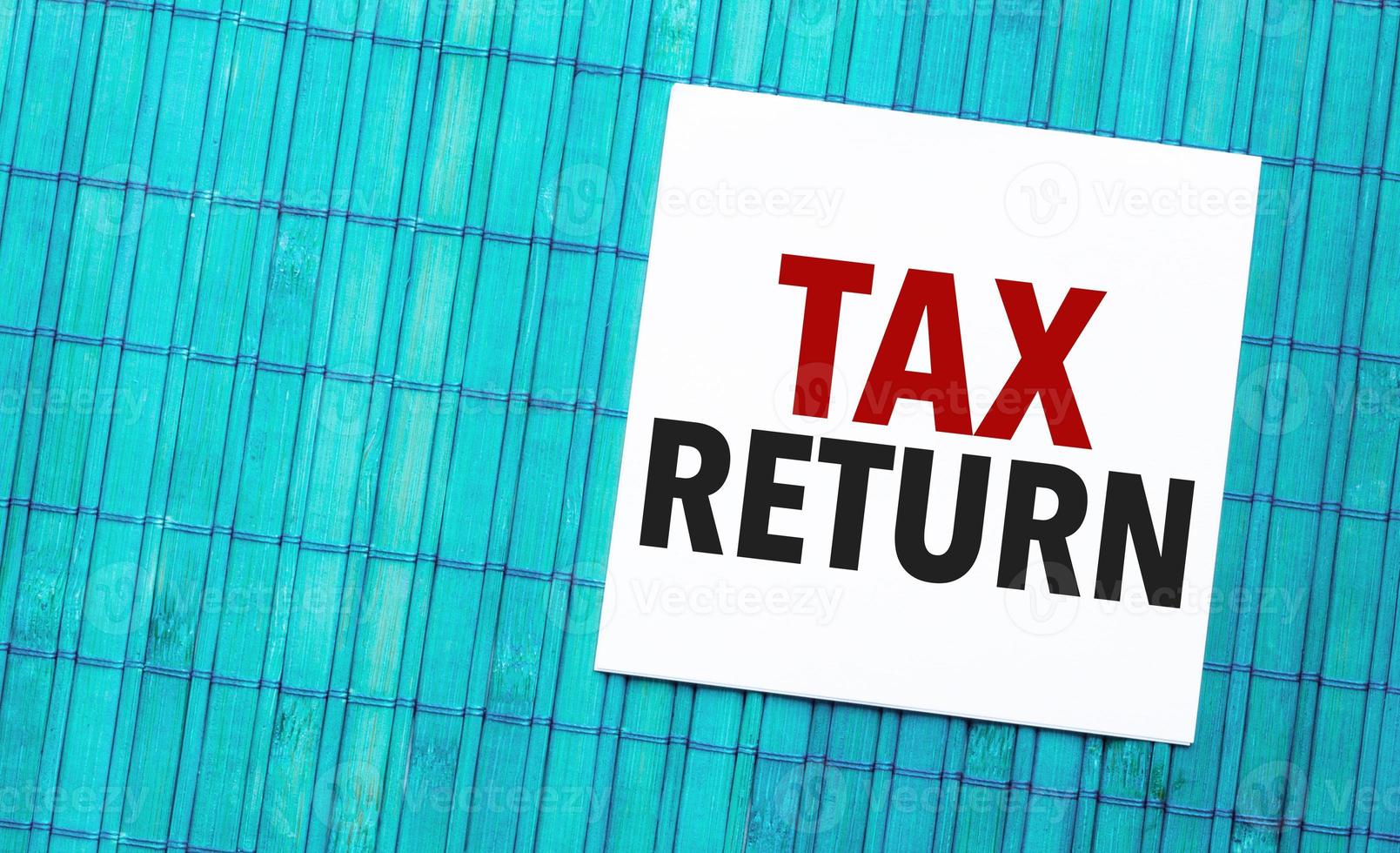 tax return word on torn paper with blue wooden background photo