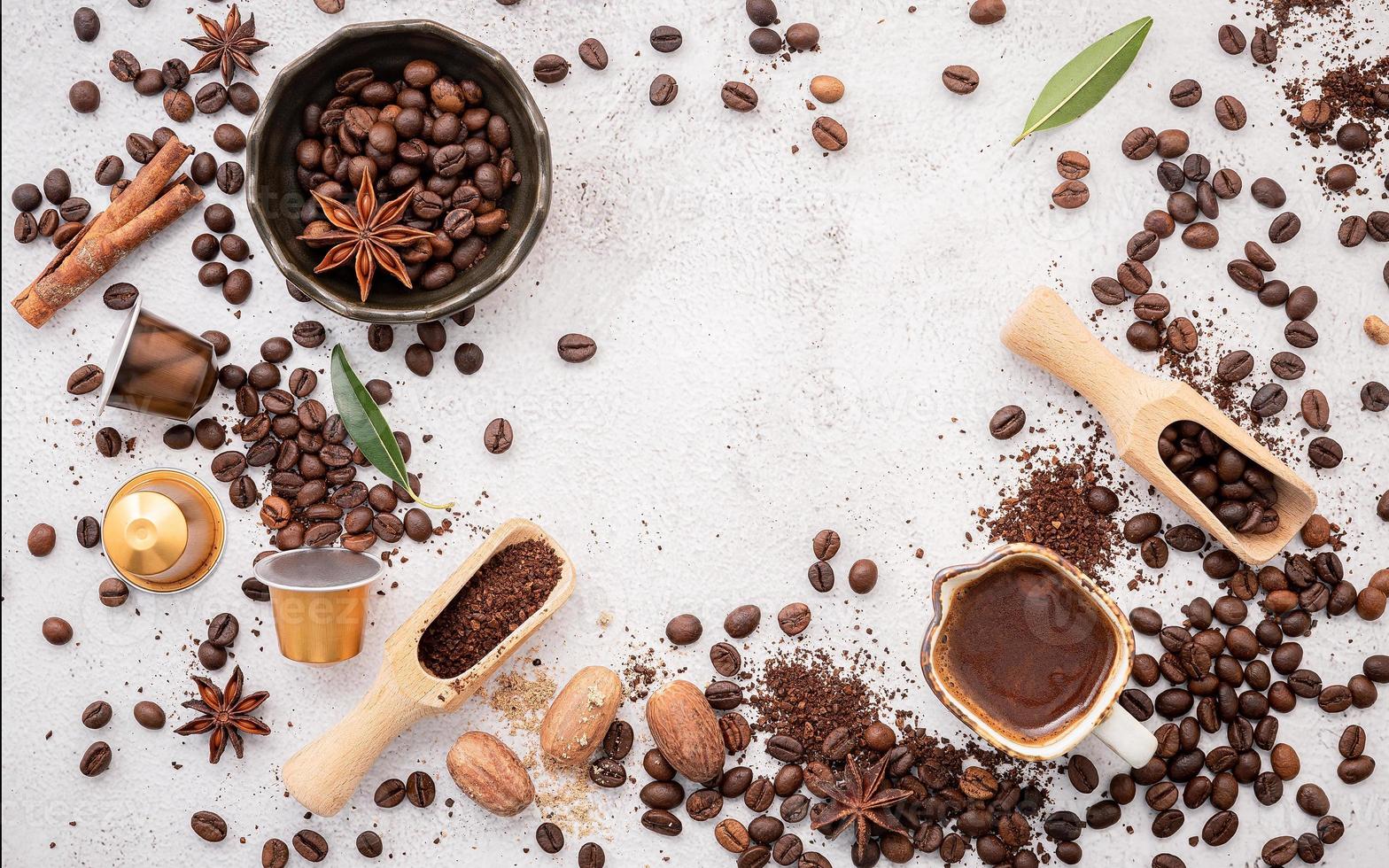 fondo de varios cafés, granos de café tostados oscuros, molido y cápsulas con cucharas colocadas sobre fondo de hormigón blanco con espacio para copiar. foto