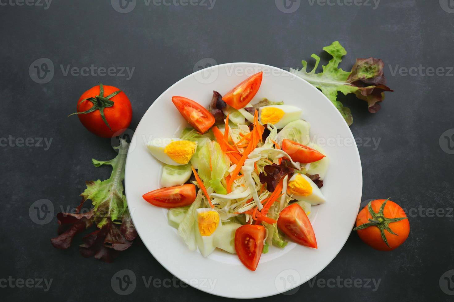 Close up of fresh salad with tomatoes and egg on black background. Healthy food concept. photo