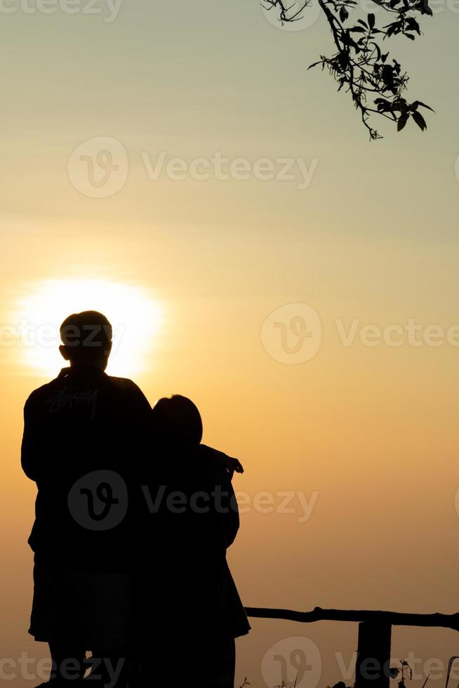 Silhouette of a young couple watching the sunset during twilight on a high mountain and embracing happily. Happy couple embracing each other with love and friendship and kindness for each other. photo