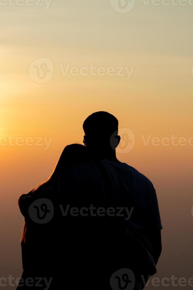 silueta de un joven Pareja acecho el puesta de sol durante crepúsculo en un alto montaña y abrazando felizmente. contento Pareja abrazando cada otro con amor y amistad y amabilidad para cada otro. foto
