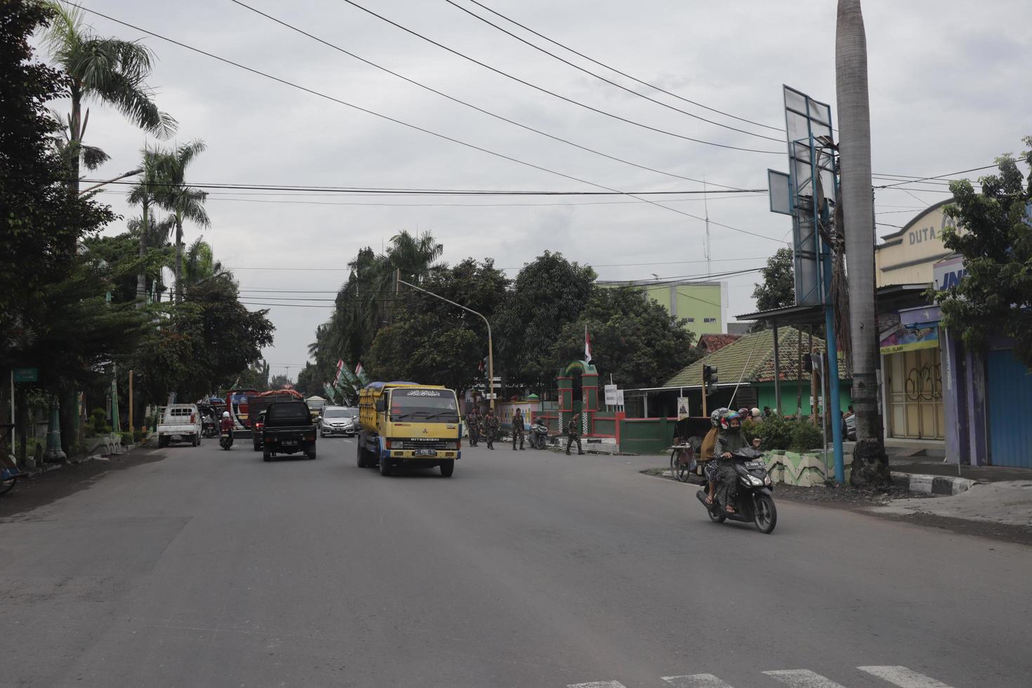 Tegal,December 2022. A group of people walked down a busy city street, using various modes of transportation along the trees and plants. photo