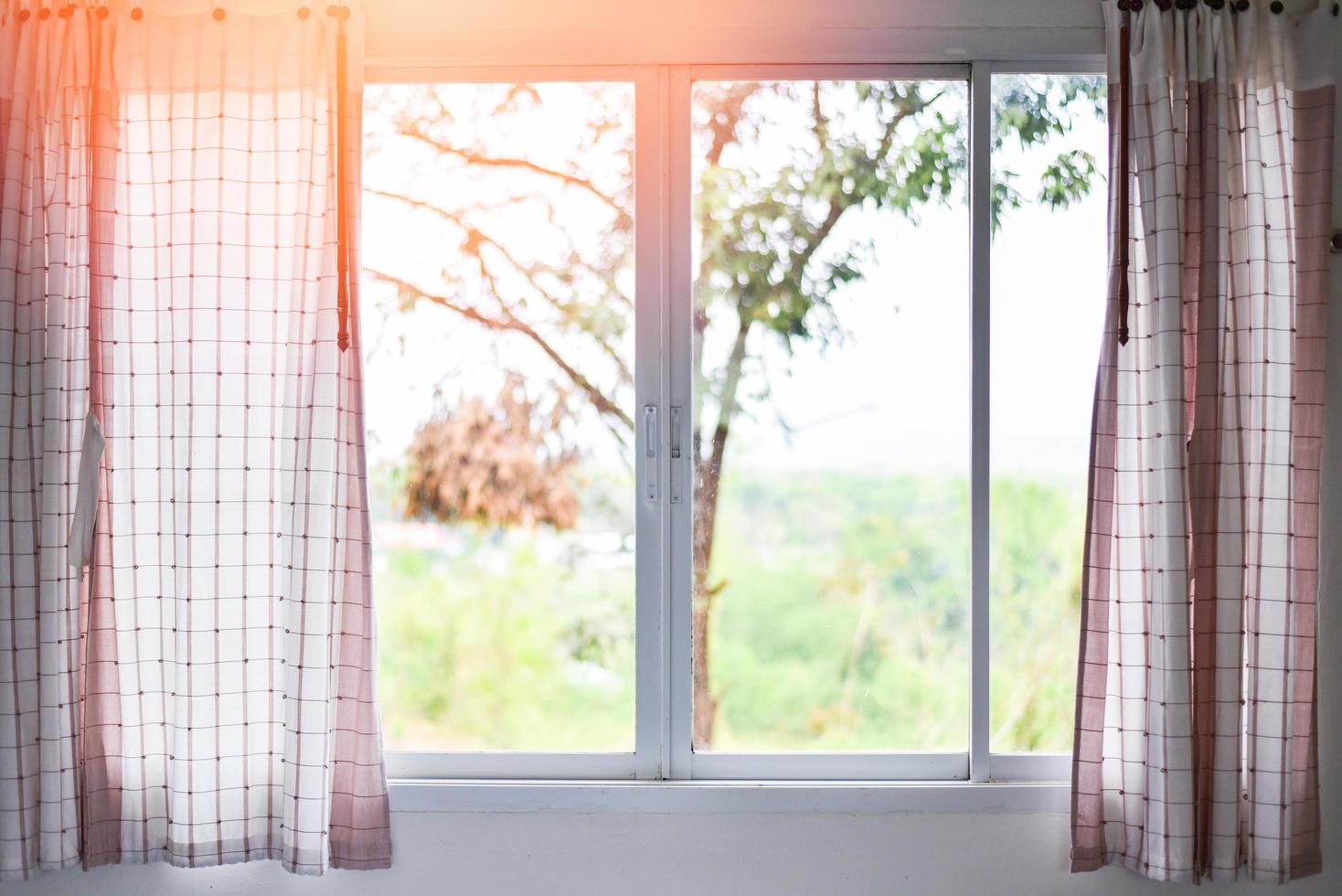 Sunlight through in room open curtains with balcony and nature tree on outside window - bedroom window in the morning photo