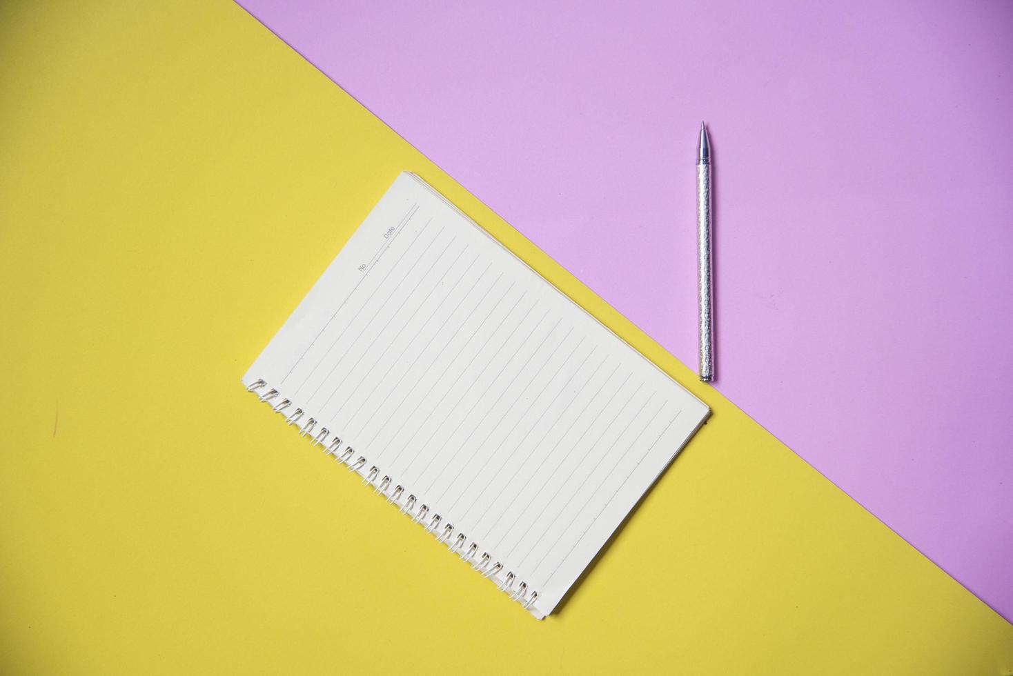 Notepad or notebook paper with pen on yellow pink background top view for education and business photo