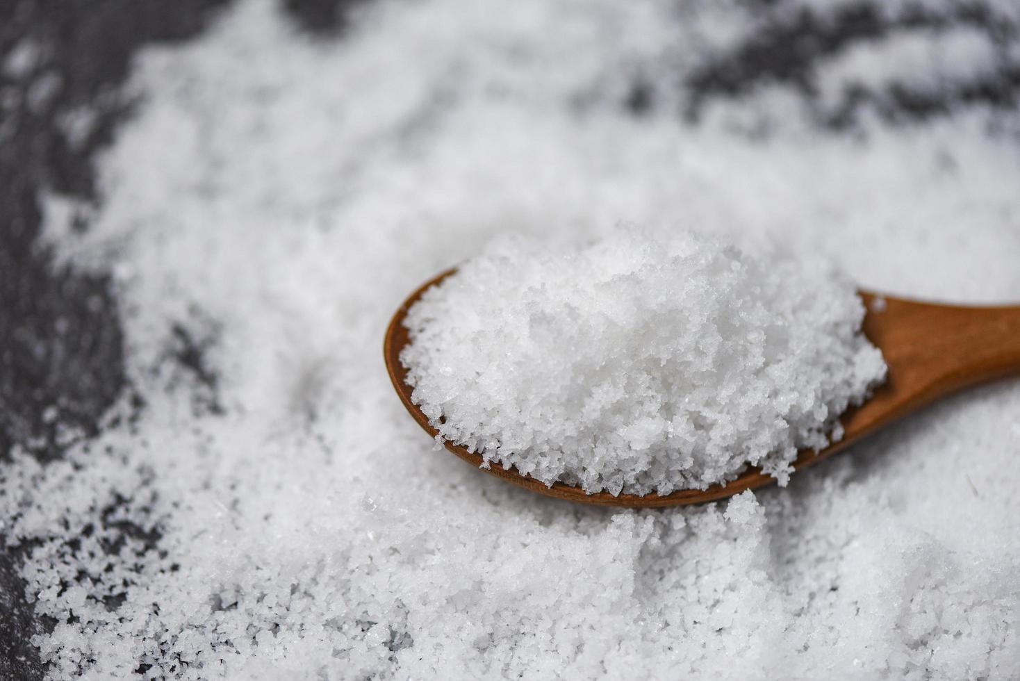 Salt in wooden spoon and heap of white salt on dark photo