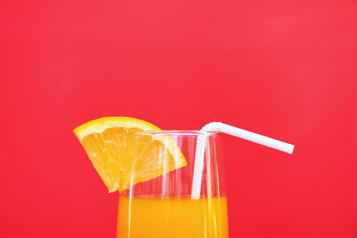 Orange juice summer glass with piece orange fruit on red background photo