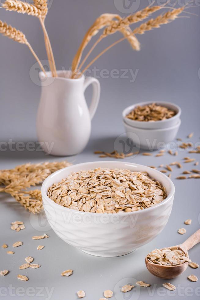 Raw oatmeal in a bowl with a wooden spoon and ears on a gray background. Vertical view photo