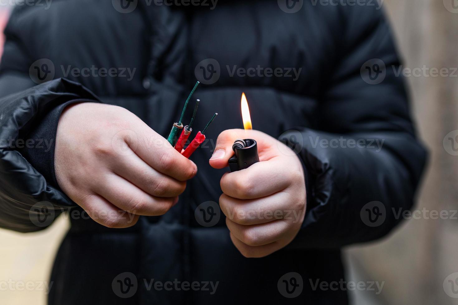 chico Encendiendo arriba varios petardos en su mano utilizando encendedor. niño consiguiendo Listo para celebracion con fuegos artificiales o pirotécnico productos . chico participación un ardiente petardo en su mano. cerca arriba Disparo foto