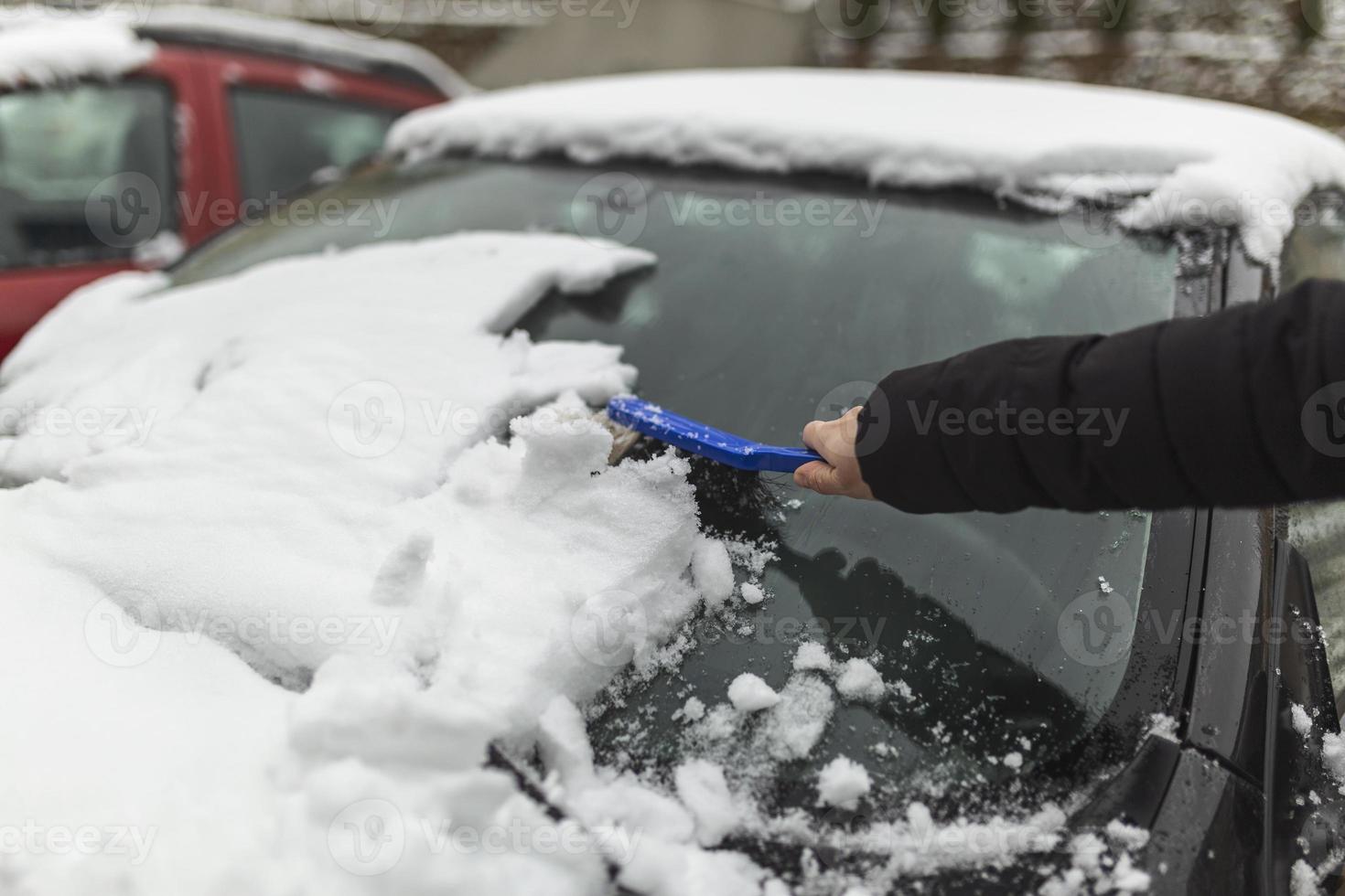 Transportation, winter, weather, people and vehicle concept - woman cleaning snow from car with brush photo