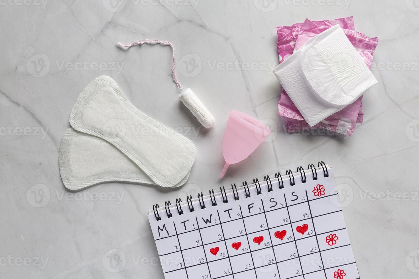 Menstrual calendar with sanitary napkins, tampons, menstrual cup on white background. Concept of critical days, menstruation photo