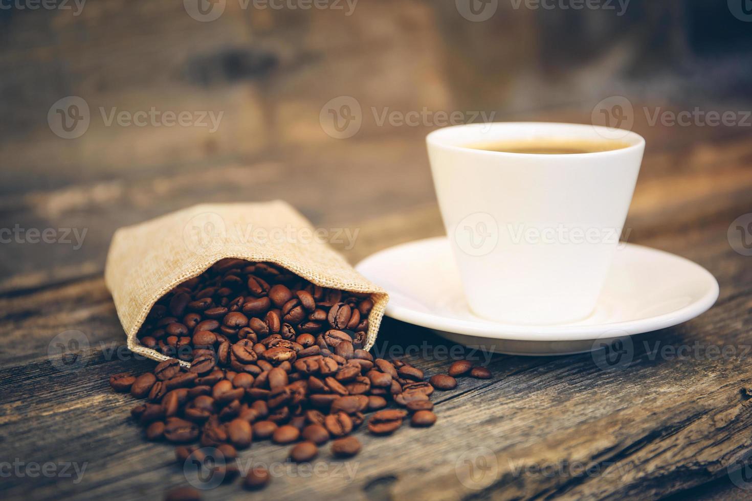 Cup and coffee beans fall out of the bag on an old wooden background. Toned image. photo