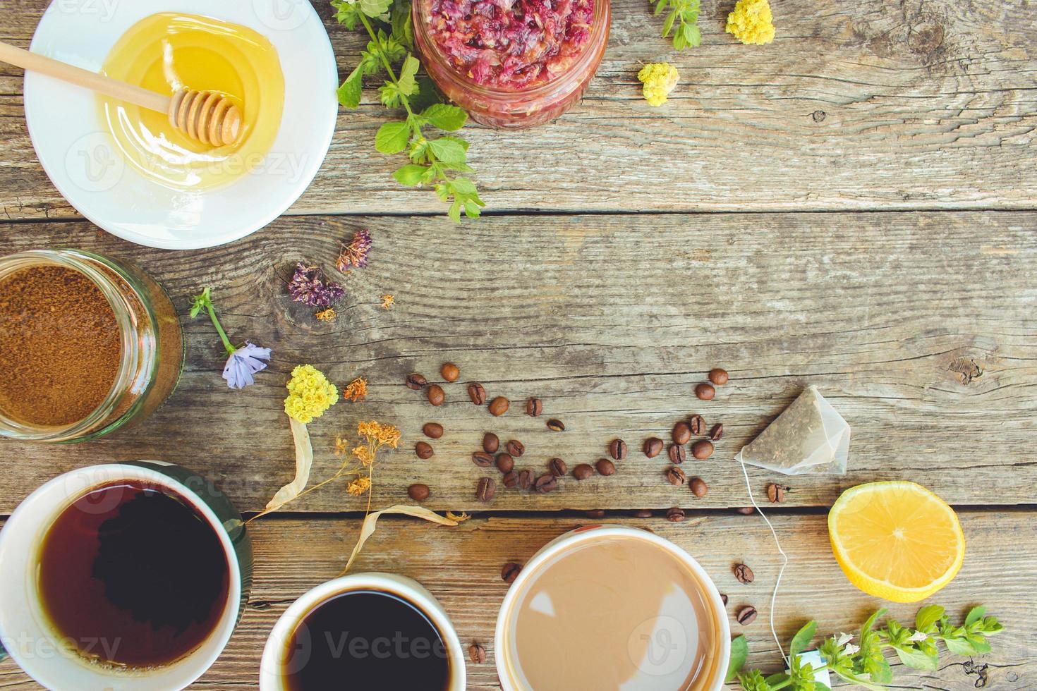 Tea, coffee, cocoa in cups, chicory, lemon, mint, jam made of rose petals, dried lime, honey on the old wooden background. Toned image. Top view. photo