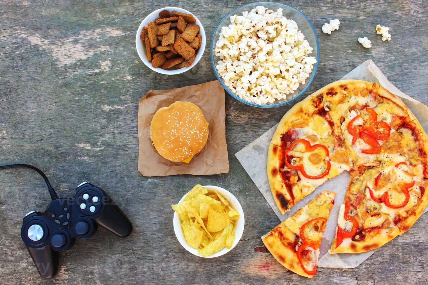 Fast food and video game controller on old wooden background. Concept of junk eating. Top view. Flat lay. photo