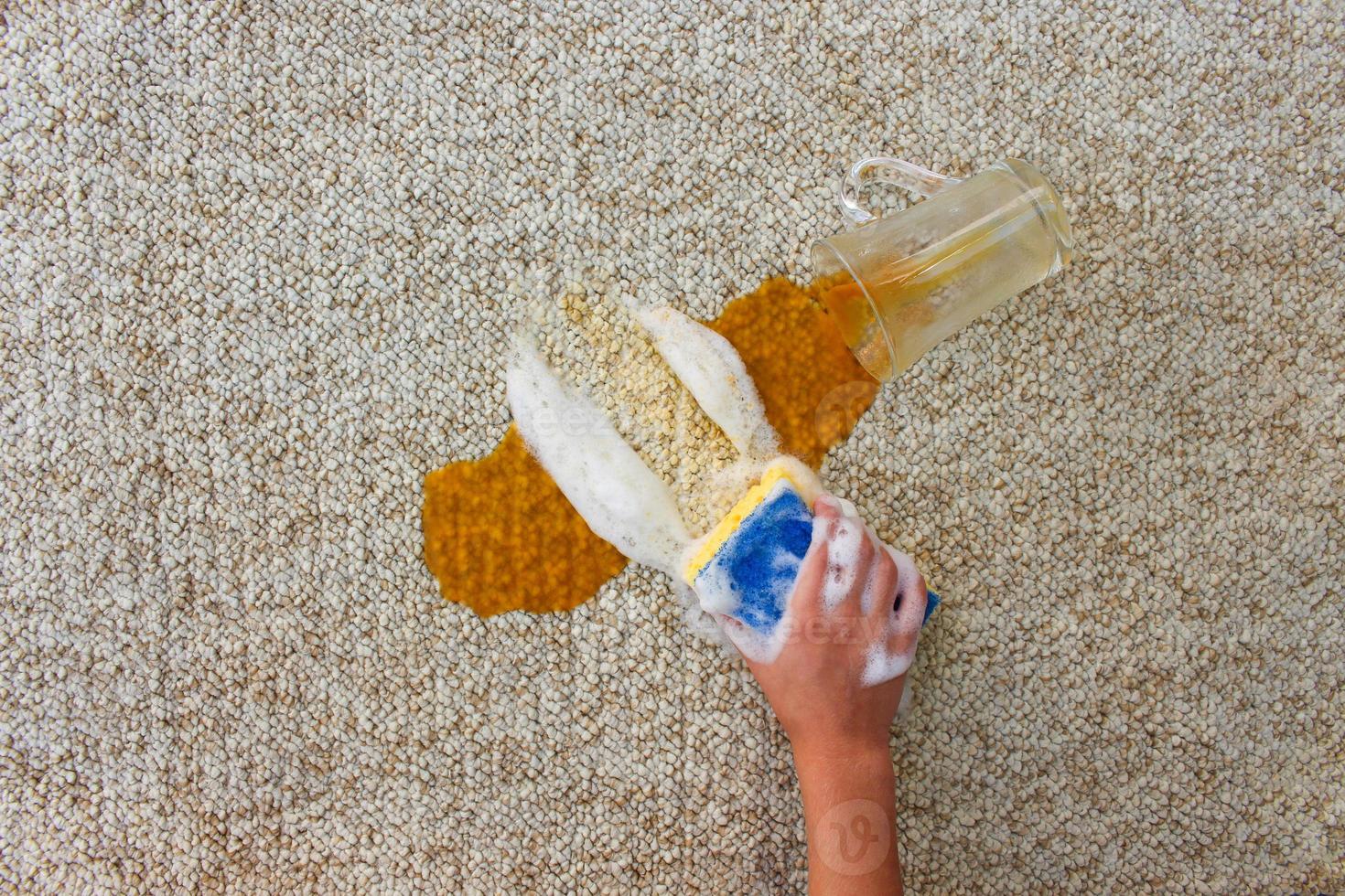 Glass of juice fell and spilled on floor. Female hand cleans the carpet with a sponge and detergent. photo