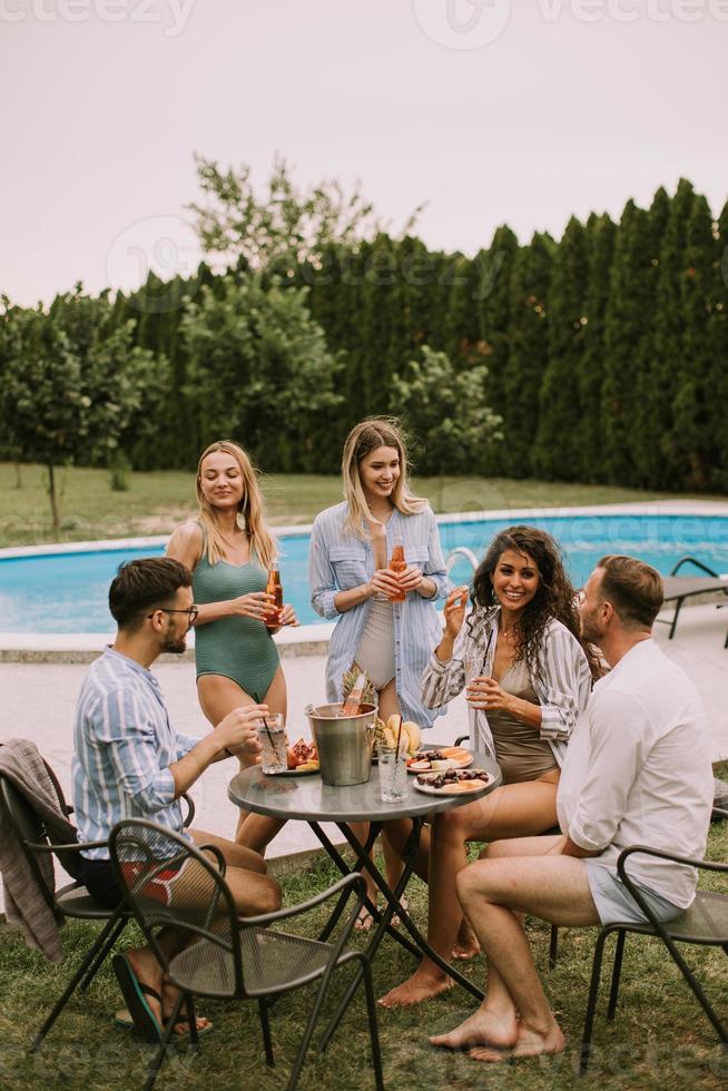 Group of young people cheering with cider by the pool in the garden photo