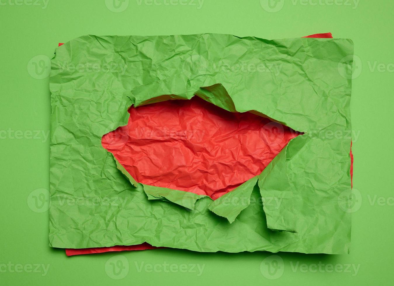Texture of crumpled green paper with torn hole and red background photo