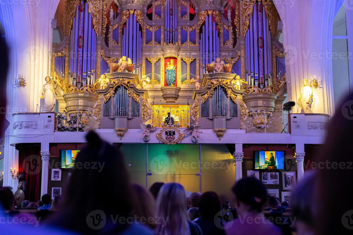 Organ music concert in cathedral. Men, women and other listeners listen to music of composer. Exciting sound. photo